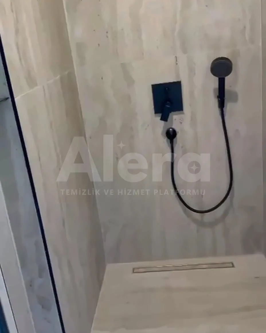 Villada traverten kaplı duş alanı, siyah armatür ve duş başlığı; temizlik sonrası görünüm